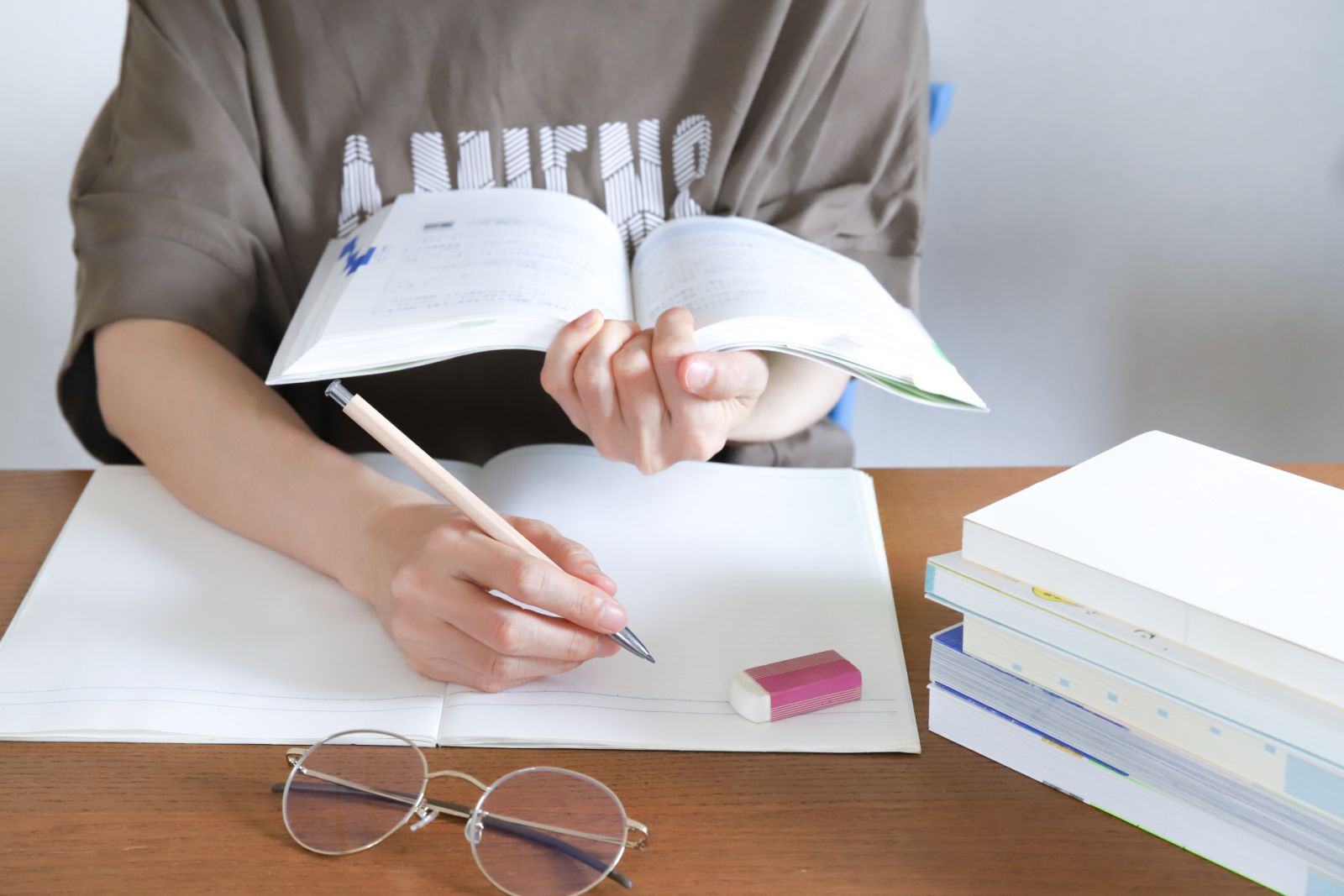 本に囲まれてノートに書き込む人の手元